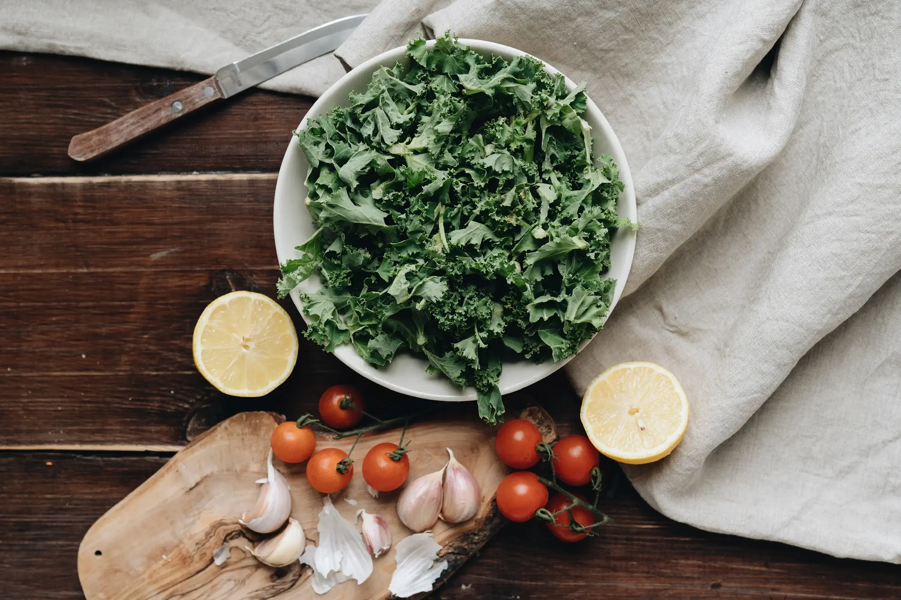 a bowl of kale with sliced lemons and tomatoes on the side